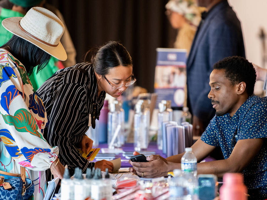 A group of individuals engages at a table during an event, with some examining materials and others conversing.